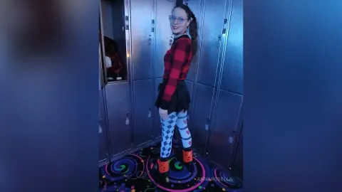Woman in red plaid top and patterned leggings posing in a locker room with a playful mood.