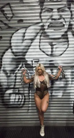 Athletic woman in a leopard print bodysuit holding metal chains in front of edgy street art graffiti.