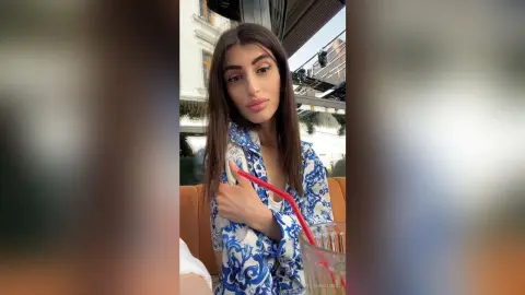Young woman in a blue patterned shirt relaxing at an outdoor cafe with a refreshing summer drink.