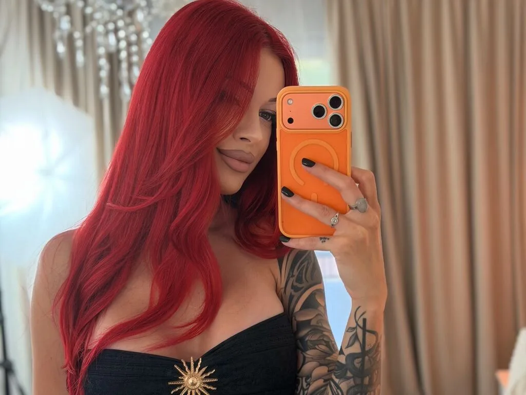 AriaVex takes a mirror selfie wearing a black strapless top, showing off her long red hair and arm tattoos.