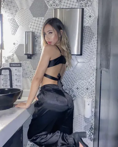 Stylish woman in a black satin outfit posing in a modern bathroom with patterned tile decor.
