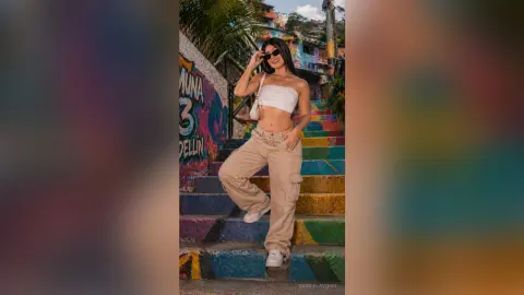 Stylish young woman in a white crop top and beige cargo pants posing on colorful outdoor urban stairs.