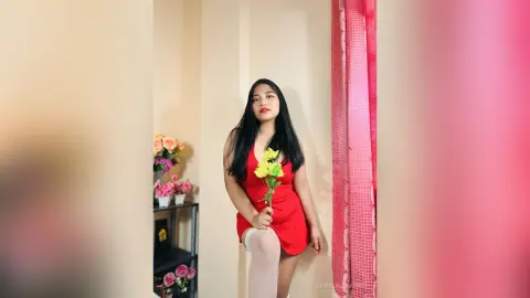Elegant woman in a red dress holding yellow flowers in a bright, minimalist indoor setting.