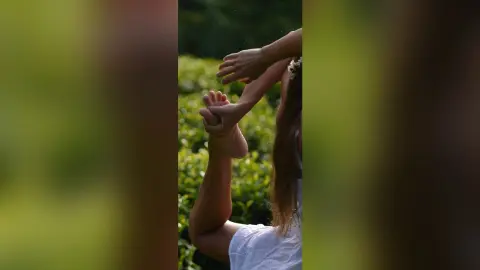 Young woman in a white dress performing a graceful yoga stretch in a lush green garden setting.