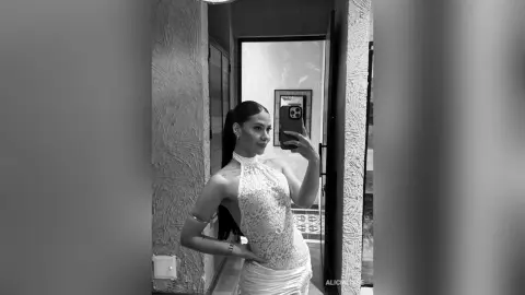Elegant woman in a white lace halter dress taking a mirror selfie in a modern minimalist hallway.
