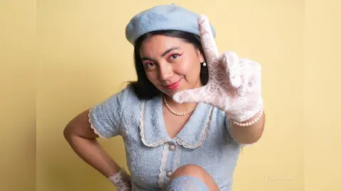 Cheerful woman in vintage light blue lace dress and white lace gloves posing against a yellow background.