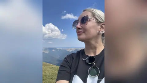 Blonde woman in sunglasses enjoying a sunny view from a scenic mountain lookout.
