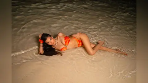 Beautiful woman in an orange bikini relaxing on a sandy beach at night under soft moonlight.