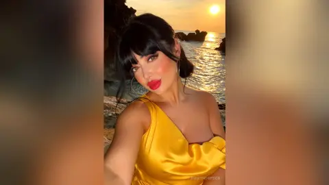 AnneThompson poses outdoors at sunset wearing a bright yellow satin dress with her black hair styled in a blunt bang fringe.