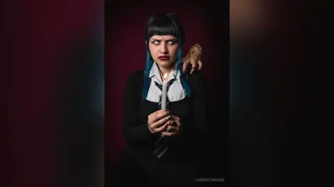 Gothic woman with blue hair and dark makeup holding a lit candle in a moody, dark setting.