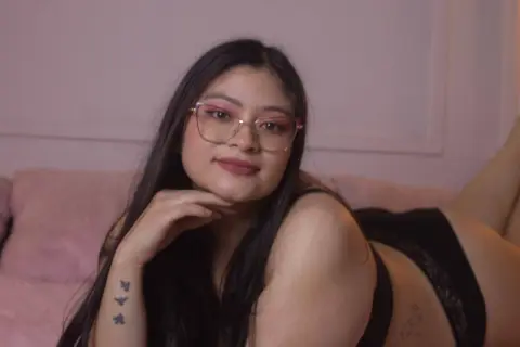 Young woman with long dark hair and glasses relaxing in black lingerie on a pink sofa in a cozy room.