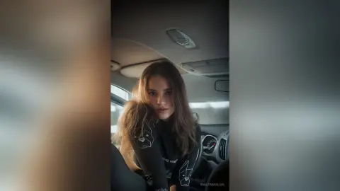 Young woman in a black long-sleeve shirt sitting in a car with a moody, cinematic aesthetic.