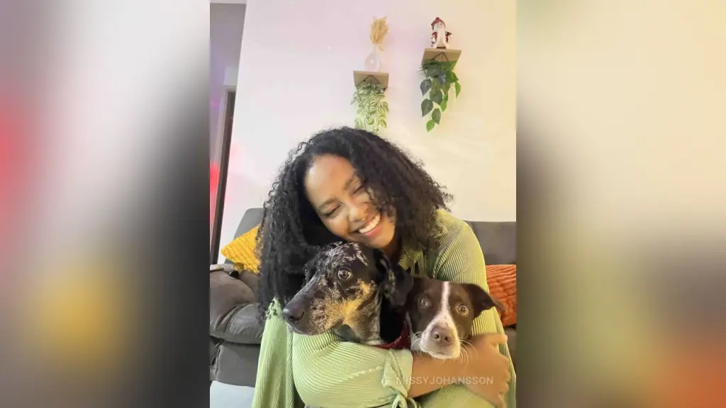 MissyJohansson — Smiling woman in a green ribbed sweater hugging a spotted dog on a cozy living room sofa.