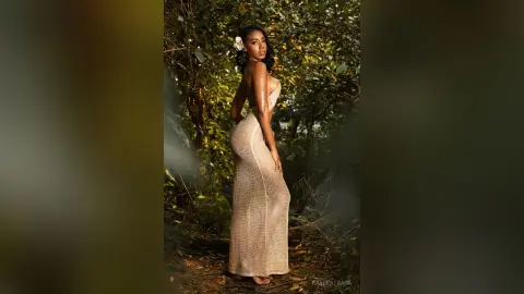 Elegant woman in a beige crochet maxi dress posing in a lush tropical forest setting.