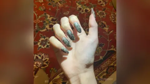 Close-up of long marble effect grey nail art on a hand held over a vintage patterned red rug.