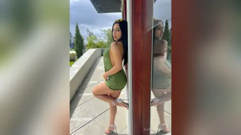 Stylish woman in a green backless mini dress posing on a sunny outdoor balcony.