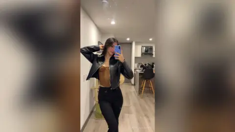 Stylish woman in a black leather jacket and brown top posing in a modern minimalist apartment.