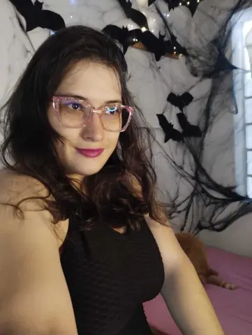 Smiling woman with glasses in a black tank top near spooky black bat decorations for a Halloween mood.