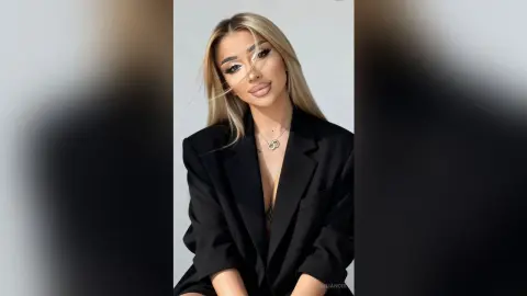 Elegant blonde woman in a chic black blazer posing against a minimalist white background.