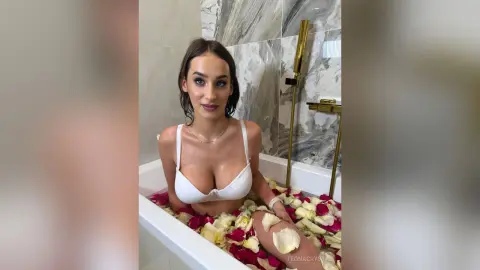 Beautiful woman in a white bikini relaxing in a marble bathtub filled with red and white rose petals.