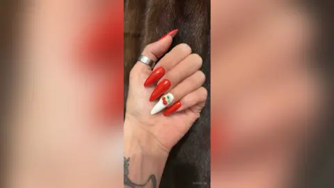 Close-up of a hand with long red stiletto nails and a white 3D cherry nail art design.