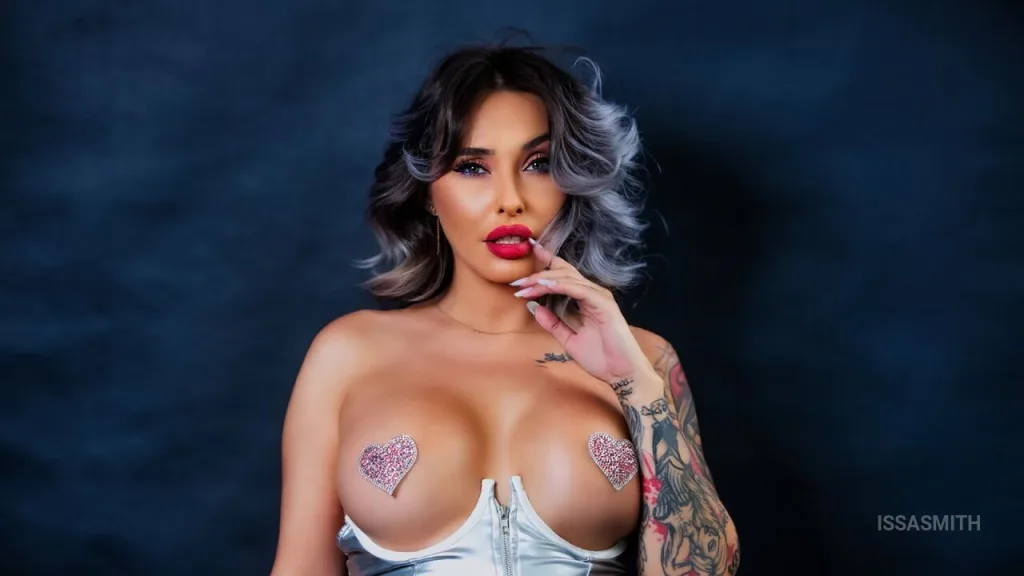 Glamorous woman in a red satin dress with tattoos posing in a luxurious, moody room with red roses.
