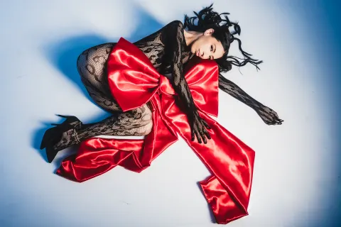 AilynHoney — AilynHoney lies on a white floor wearing black lace lingerie and a large red satin bow.