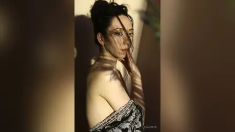 Moody portrait of a woman with dark hair and winged eyeliner wearing a patterned black and white dress.