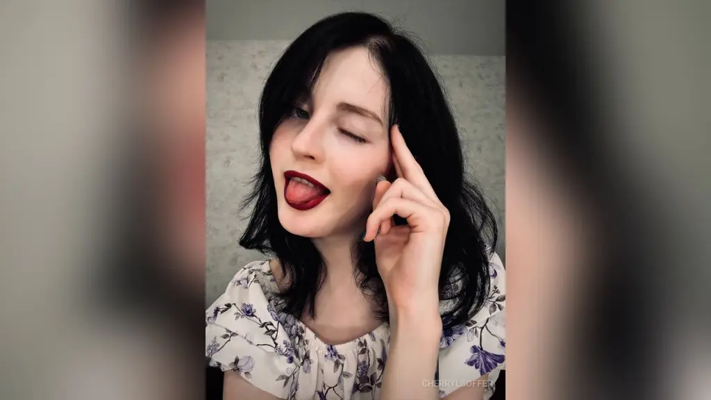 Woman with dark hair and red lipstick wearing a black outfit taking a moody mirror selfie indoors.
