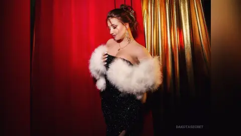 Elegant woman in a black sequin dress and white faux fur stole posing against red and gold curtains.