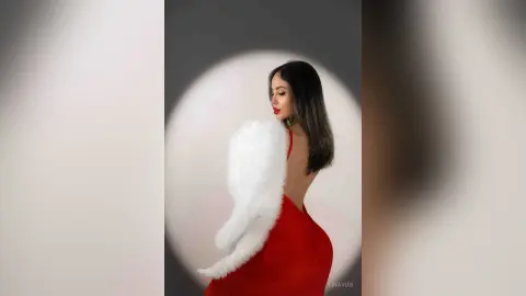 Elegant woman in a red evening gown and white faux fur stole posing against a studio spotlight background.