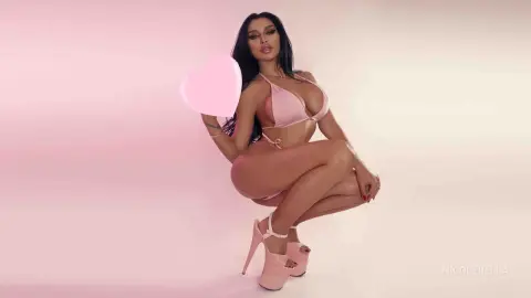 NicoleBella poses in a pink bikini and matching high heels against a soft pink background.