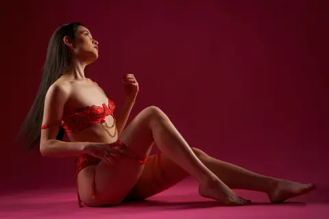 Elegant woman in red lace lingerie sitting against a moody crimson background.