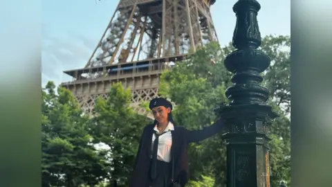 Stylish woman in a black blazer and tie posing by a vintage lamp post with the Eiffel Tower in Paris.