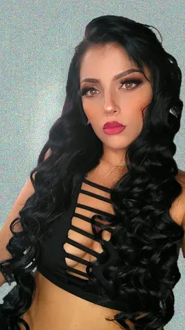 Glamorous woman with long wavy black hair wearing a black cutout crop top against a glittery background.