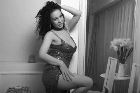 Curvy woman in a sparkling sequin cocktail dress posing in a bright, modern room.
