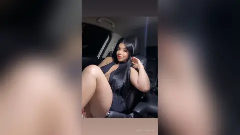 Smiling woman in a black bodysuit sitting in a car interior with a relaxed mood.