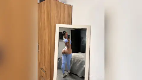 Curvy woman in light blue yoga set taking a mirror selfie in a bright bedroom.