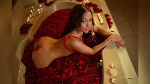 Sensual woman in red lingerie relaxing in a bathtub filled with red rose petals by candlelight.