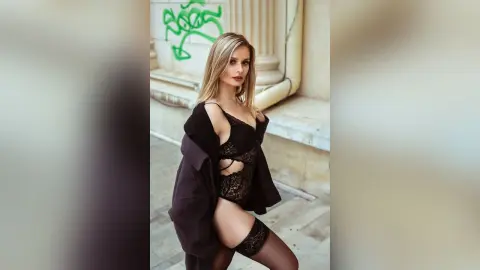 Gia poses in black lace lingerie and a dark open robe against a stone wall and pillar.