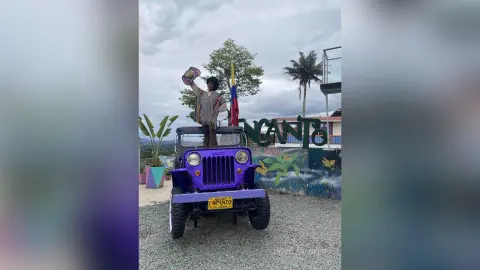 Woman in a striped boho dress holding a hat while sitting on a purple Jeep in front of an Encanto sign.