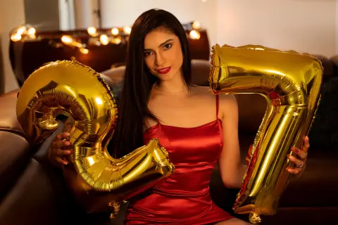 Young woman in a red satin dress holding large gold number 27 balloons for a birthday celebration.