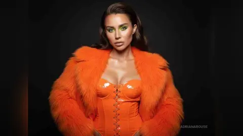 Glamorous woman in bright orange faux fur coat and matching corset bodysuit posing against a black background.