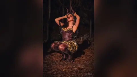 JessieLiu poses in a dark forest wearing a brown leather bustier and furry skirt with matching horns.
