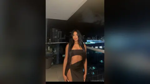 Glamorous woman in a sleek black cutout dress posing on a city balcony at night.