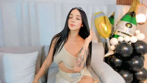 Young woman in a beige outfit wearing a tiara, celebrating a birthday with champagne and balloons.