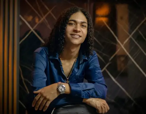 KylePresly smiles while wearing a blue button-down shirt and a gold chain necklace.