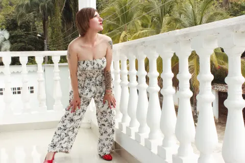 Woman in floral strapless jumpsuit sitting on a white balcony overlooking tropical palm trees.