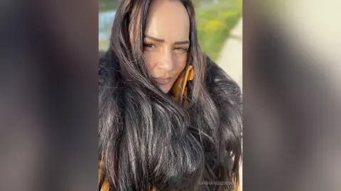 Smiling woman with long dark hair wearing a mustard yellow jacket in a bright outdoor setting.