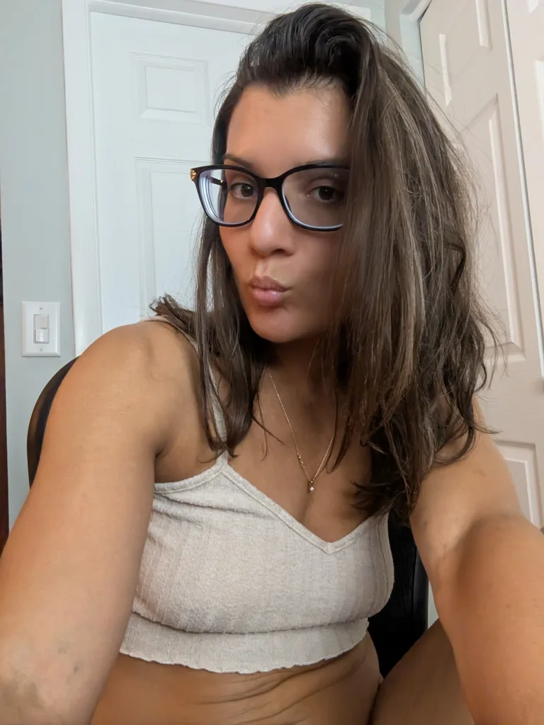 Smiling brunette woman in a beige sleeveless top relaxing in a bright modern bedroom.